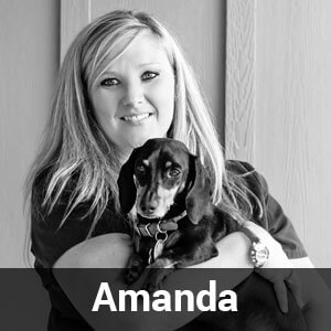 A black-and-white image shows a woman with long, blonde hair smiling at the camera. She is holding a small dog. The name "Amanda" is overlaid at the bottom of the image.