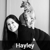 A woman with long, dark hair is smiling, and there is a cat sitting on her shoulder. The image is in black and white. The caption at the bottom reads "Hayley.
