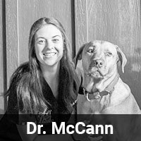 Woman smiling next to a dog in front of a wooden wall. Text overlay reads "Dr. McCann.