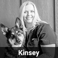 A black and white image of a person with long hair smiling and posing beside a dog. Both are looking at the camera. The name "Kinsey" is displayed in bold text at the bottom of the image.