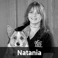 A woman with long hair smiles while holding a dog with large ears. She wears a shirt with a logo that reads "360° Pet" and stands against a wooden backdrop. The name "Natania" is written at the bottom of the image.